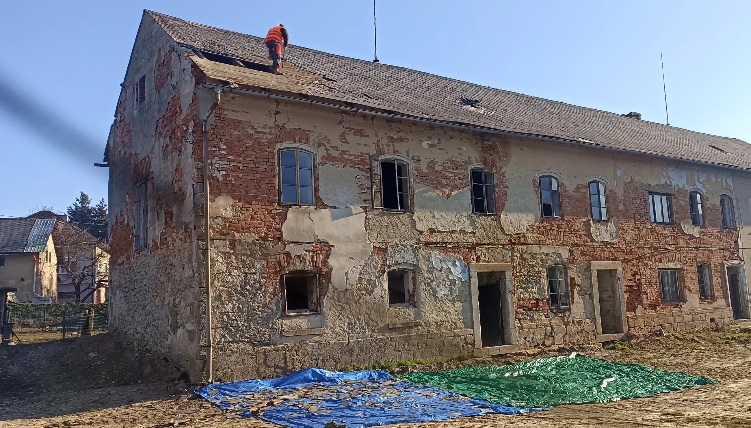 Starý zděný dům před demolicí, pracovník na střeše