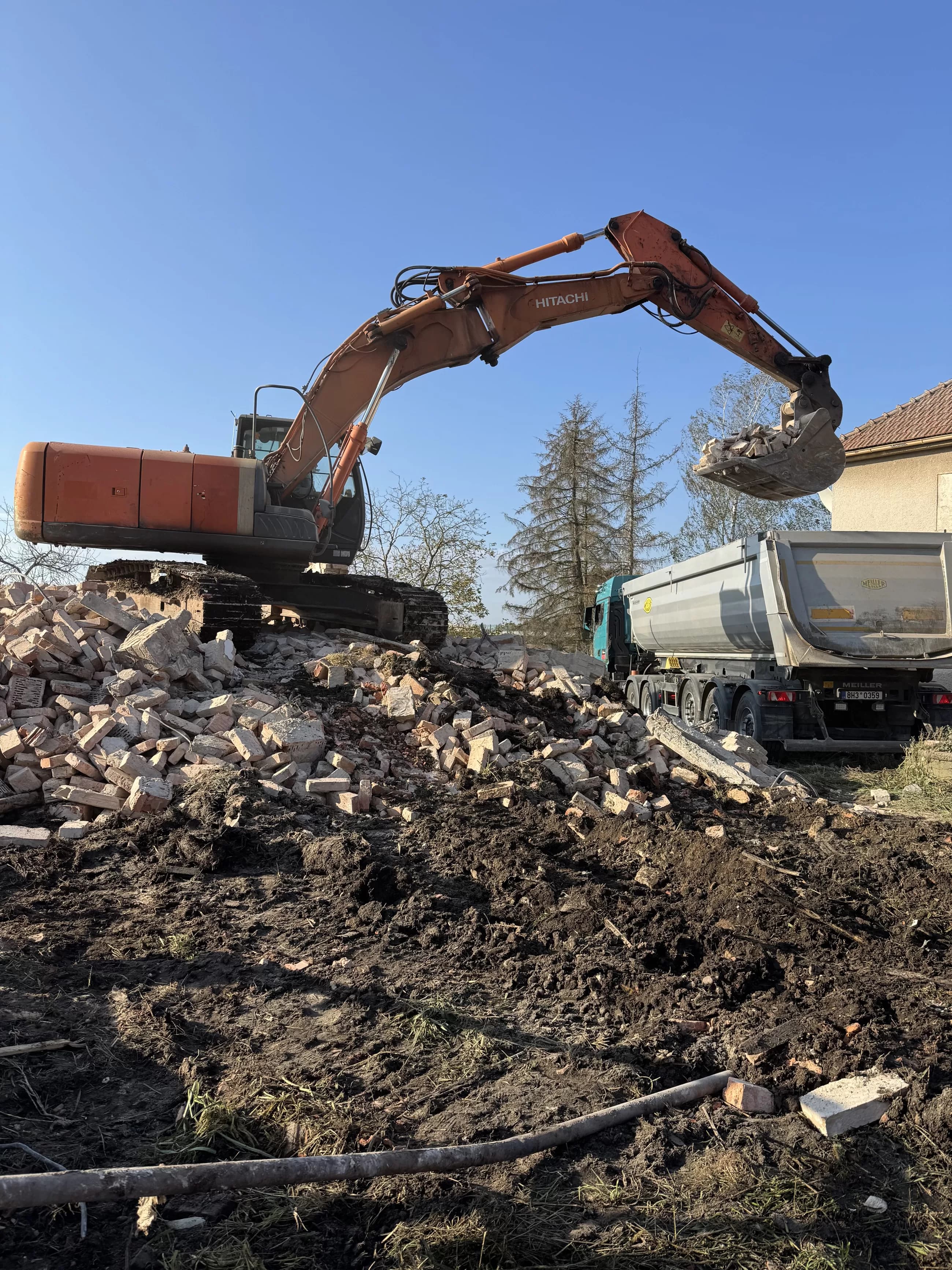 Bagr nakládá cihlovou suť z demolice do nákladního auta