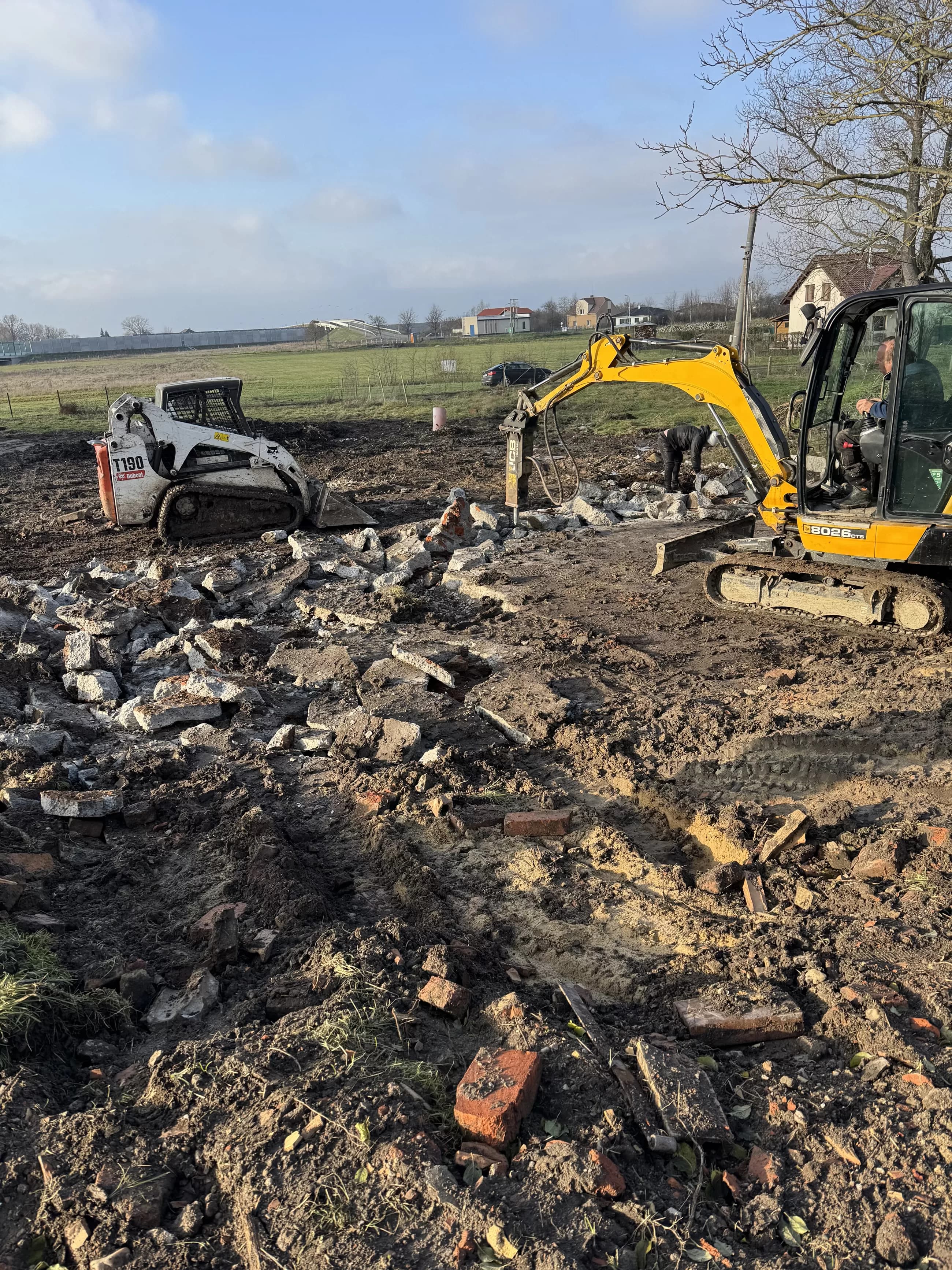Bagr s bouracím kladivem a nakladač při demolici základů